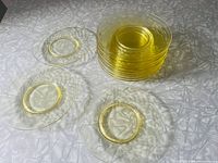 Stack of twelve yellow translucent luncheon plates with pressed diamond quilted pattern and central rings, displayed on a light textured fabric.