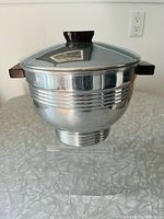 Front side view of the aluminum ice bucket with Bakelite handles and knob. Shiny finish with horizontal ridges and small dent on lid visible.