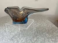 Side angled view of freeform smokey brown and blue glass ashtray showing elongated curved shape and heavy solid base.