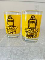 Two clear glass shot glasses with yellow background and black Aspirin bottle illustration on front, labeled 'Chemical Hall of Fame'