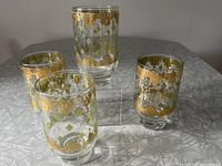 Four footed tumblers arranged with detailed gold and green diamond design in Hollywood Regency style.