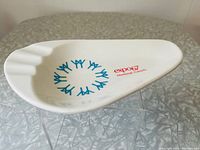 Top view of white plastic Expo67 souvenir ashtray showing blue logo and red text.