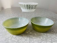 Three Fire-King bowls displayed on table, two avocado green and one white with green Birch Stripes pattern