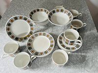 Full view of the set showing grouped plates, bowls, cups, and saucers with geometric patterned rims.