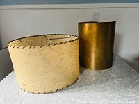 Two vintage lampshades shown side by side on a table surface, displaying shape and size comparison.