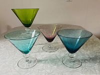 Photo showing all four jewel-toned martini glasses in green, purple, light blue, and dark blue arranged on a white textured surface.