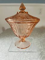 Front view of vintage pink glass candy dish with lid, showing embossed floral patterns and finial knob.