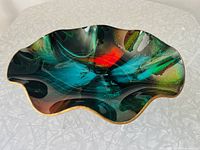 Top view of the decorative dish showing multicolored swirls of blue, green, and red with a wavy edge and glossy finish.