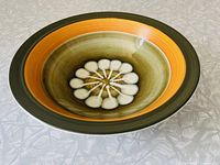 Top view of the ceramic bowl showing interior floral design and graduated earth-tone glazes from brownish green to mustard yellow and green outer rim.