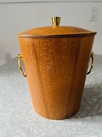 Front side view of the teak wood ice bucket with brass-colored metal handles and a matching teak lid with brass knob.
