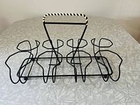 Front angle view of vintage black metal beverage caddy showing the wireframe holders for eight glasses and the white woven vinyl wrapped handle.