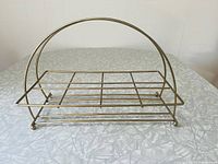 Photo of vintage metal beverage caddy showing rectangular wire grid base, arching brass-tone handle and feet.