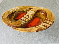 Oval vintage ceramic ashtray viewed from side angle showing rust burst glaze and segmented troughs for cigarette rests.