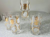 Four Federal Glass vintage hi-ball glasses standing together on a white surface, showing gold and white leaf design.