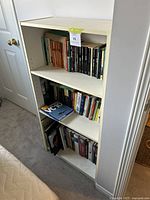 White wooden bookshelf filled with multiple books organized across three shelves showing the entire lot