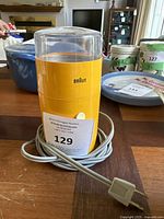 Front view of vintage yellow Braun coffee grinder with clear plastic lid, electrical cord coiled around base.