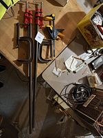 Photo of 4 clamps on wooden table showing large red C-clamps, smaller red C-clamp and black/yellow quick-release clamp