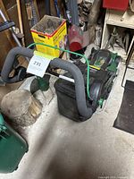 Electric green and black Certified lawn mower with ergonomic handlebar, rear grass collection bag, shown from front angle on concrete floor in shed.