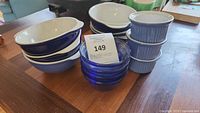 Image showing six Emile Henry cobalt blue soup/cereal bowls with lug handles, white interiors, stacked along with four translucent blue glass bowls and three cobalt blue ribbed ceramic ramekins.