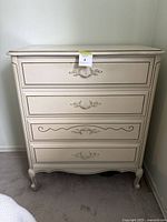 Front view of antique French Provincial style dresser showing four drawers with decorative handles and carved details, cream painted finish.