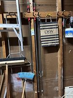 Wooden wall with hooks holding the two large metal bar clamps with red screw handles. Shows full length and setup.