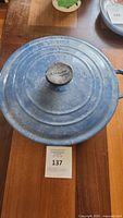 Top view of blue round Le Creuset Dutch oven with lid on wooden table, showing overall exterior condition.
