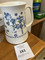 Photo showing the pitcher jug with a handle, decorated with blue floral motifs and a female figure on white ceramic.