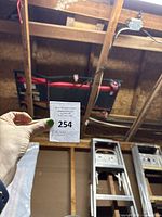 Hand holding auction lot number in front of the mechanics creeper cart attached to the ceiling showing size and context.