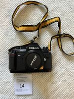 Front view of Nikon N2000 film camera with Nikon body cap and yellow/black strap attached.