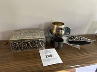 Photo of all metal items displayed on a wooden surface, showing decorative rectangular box, goblet, bell, cups, and dish.