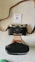 Camera inside leather carrying case with front cover open and visible wear on case; showing camera body and part of strap.