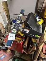 Top view of a blue metal toolbox filled with various hand tools including a spirit level, adjustable wrench, files, clamps, a small plastic tool case, sanding paper, and a measuring tape.
