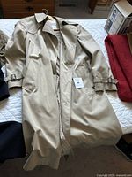 Full view of beige London Fog trench coat with sleeves showing buckle straps and checked lining partially visible.