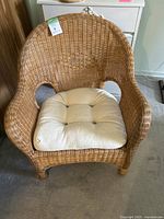 Front view of the wicker chair with the beige cushion placed on the seat, showing overall condition and shape.