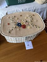 Closed white wicker sewing basket with embroidered floral fabric lid