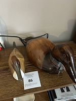 Pair of wooden duck decoys on a wooden shelf, one larger with a fabric collar and one smaller carved and painted decoy.