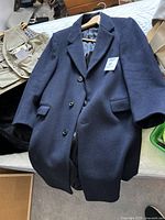 Navy blue wool jacket laid out on a bed, showing full front with three buttons and two front pockets. Jacket tag shows 'Eaton' and size large.