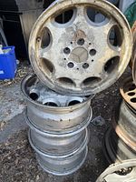 Stack of four 15-inch Mercedes alloy rims with visible corrosion and wear, side view showing rim condition.