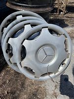 Four Mercedes hubcaps stacked showing star logo and one cracked hubcap.
