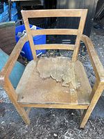 Front view of the solid oak office chair showing horizontal slats, armrests, and worn seat surface with peeling damage.