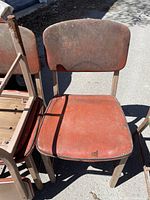 Front view of one metal chair showing reddish seat and backrest with heavy rust and wear.