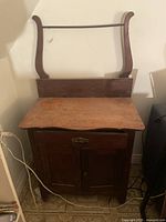 Antique wooden washstand viewed from the front showing drawer, cabinet door, and towel bar