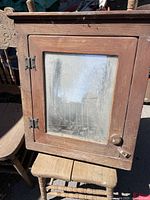 Front view of antique wood cabinet door with glass window, wooden knob, and metal hinges.
