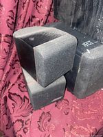 Photo showing Bose cube speakers with black fabric grills stacked on Bose bass reflector, placed on a patterned fabric background.