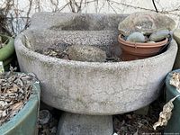 Side angle view of the salvaged concrete factory sink fountain showing textured surface and basin with leaves and stones inside.