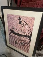 Photo of a large wooden picture frame with glass and matting showing silhouette artwork of a person and birds against a patterned background.