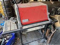 Closed red Weber BBQ grill with side shelves and wheels shown from front