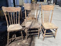 Front view of the three antique wooden pressback chairs placed outside, showing carved wooden details and turned legs.