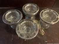 Four vintage clear glass shrimp cocktail servers arranged in a square on a dark surface, each with decorative oval cut-outs on the bowl rims and pedestal base visible.