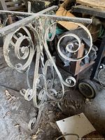 Close-up photo showing the curved scrollwork and condition of metal table base, highlighting peeling paint and surface corrosion.